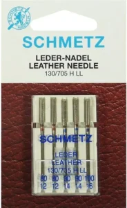 Leather sewing machine needle with wedge-shaped tip next to faux leather fabric